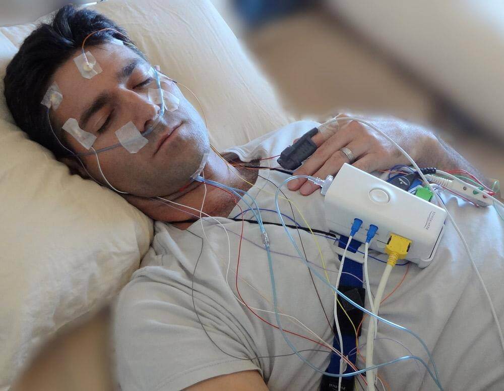 Patient undergoing polysomnography sleep study test with monitoring sensors for sleep apnea diagnosis
